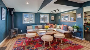 A cozy living room with a fireplace, a large window, and a seating area with a rug and ottomans. - Loyal Duke Lodge (Salida)