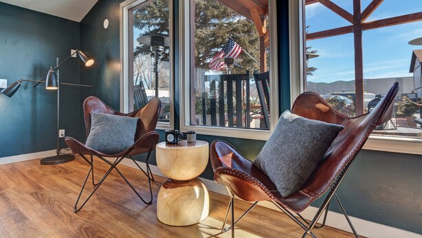 A room with two leather chairs, a wooden coffee table, and a large window with an American flag. - Loyal Duke Lodge (Salida)