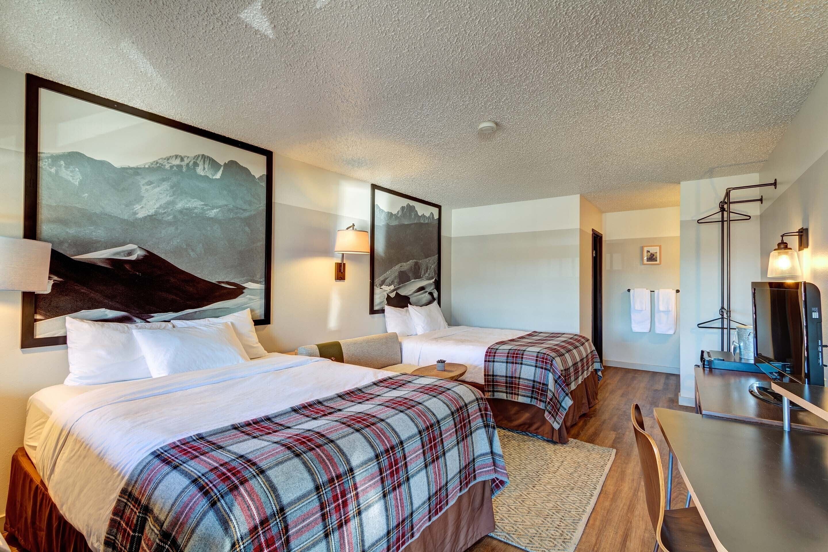Quarto de hotel com duas camas, uma escrivaninha, televisão e quadros na parede.