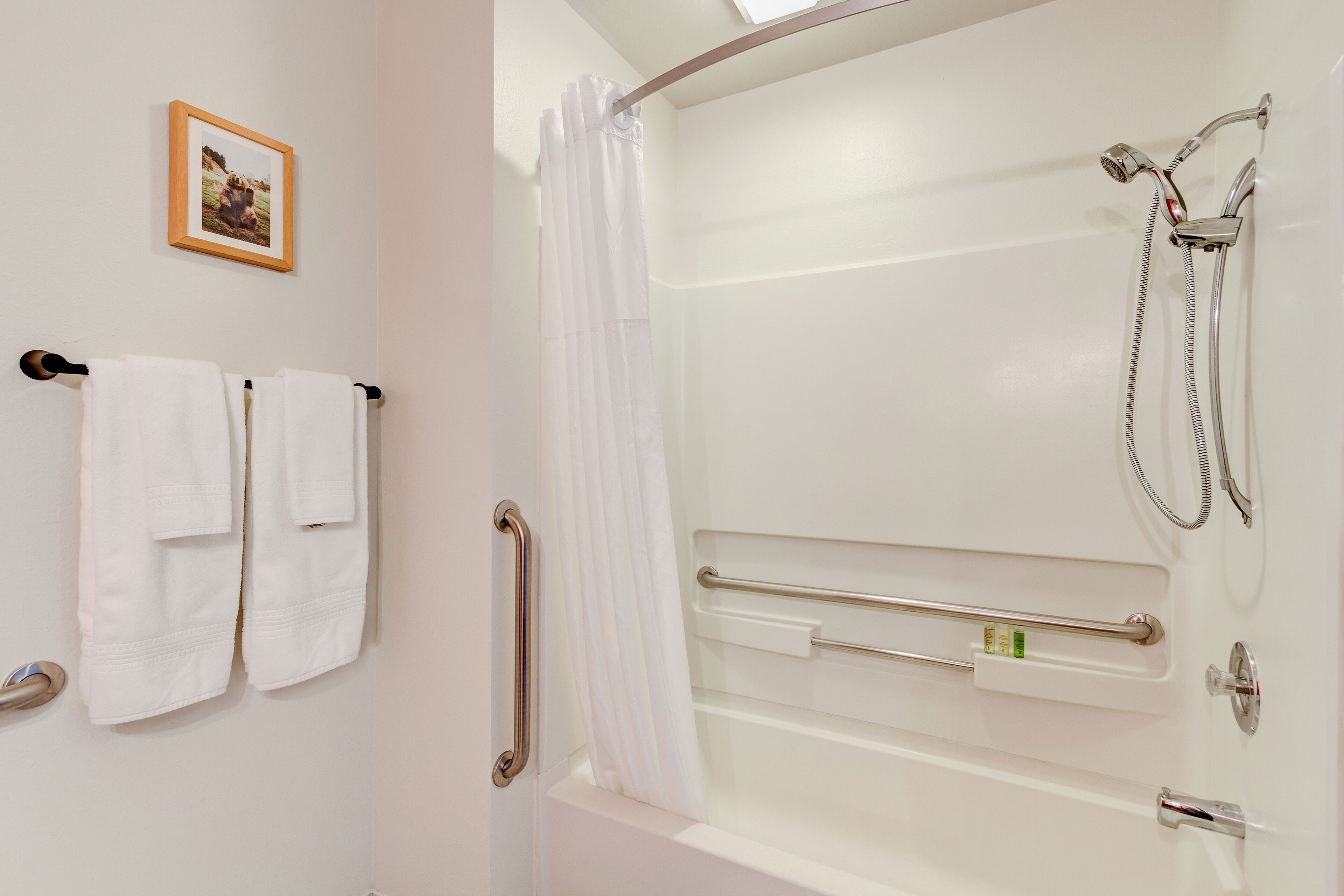 Bagno con doccia, maniglie di sostegno e porta asciugamani con asciugamani.