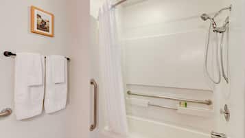 A bathroom with a shower, grab bars, and a towel rack with towels.