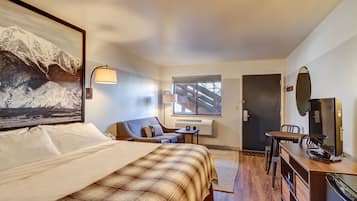 Habitación de hotel con cama, escritorio, silla, televisor y ventana con vistas a montañas.