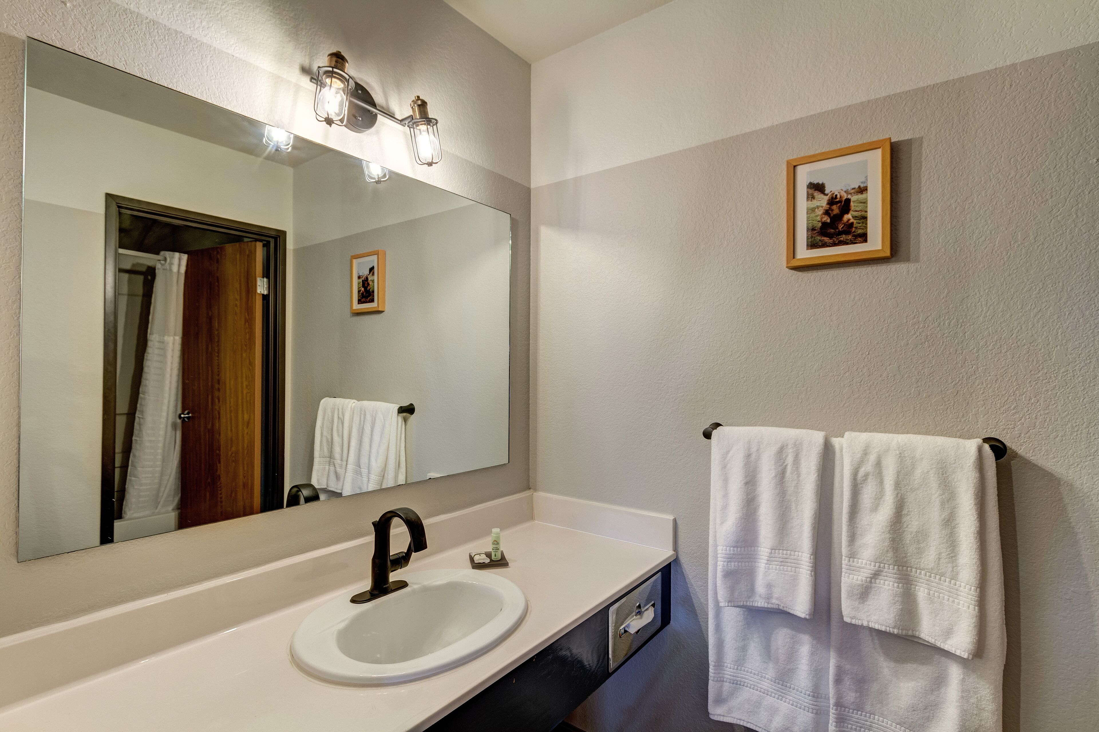 Une salle de bain avec un grand miroir, un lavabo et deux serviettes suspendues à un porte-serviettes.
