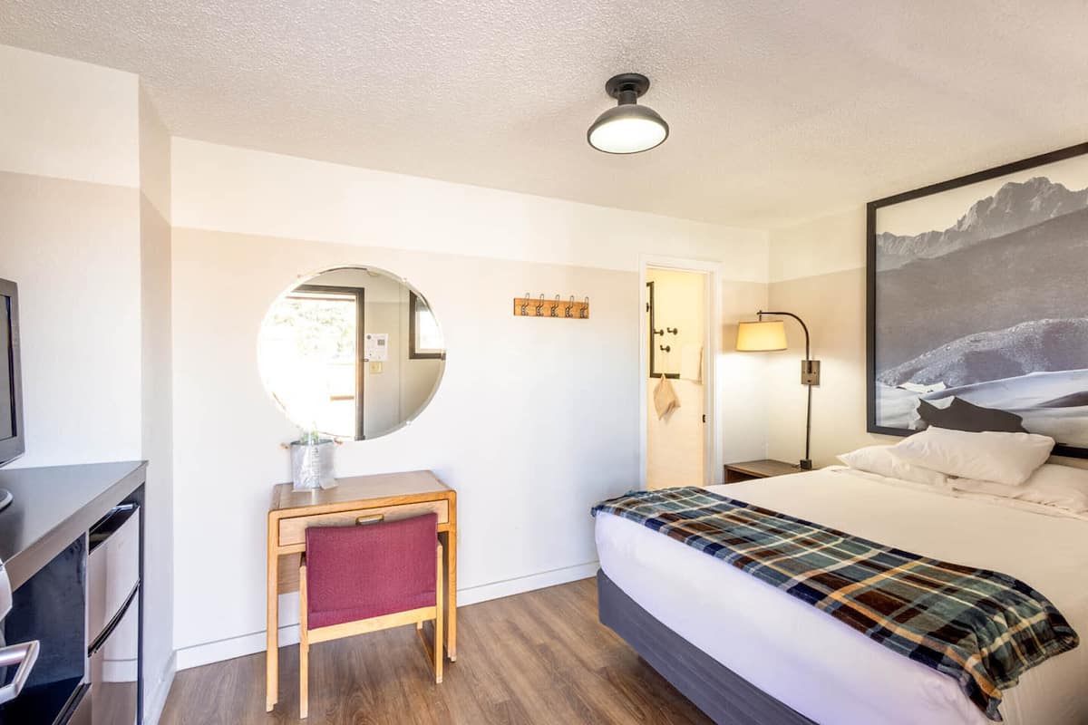 Une chambre d’hôtel avec un lit, un bureau, une chaise, un miroir, une lampe et un tableau au mur.