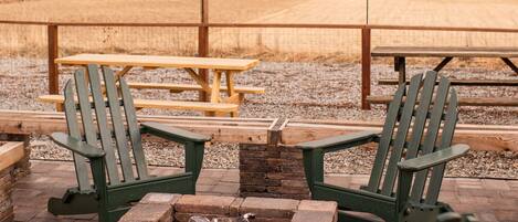 A patio with Adirondack chairs, a fire pit, and a picnic table.