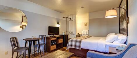 A hotel room with a bed, a sofa, a desk with a chair, a television, and a mirror.