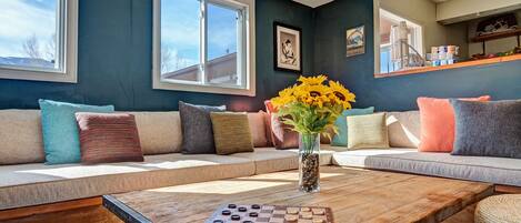 A living room with a sofa, a coffee table with a chessboard, and a vase with flowers.