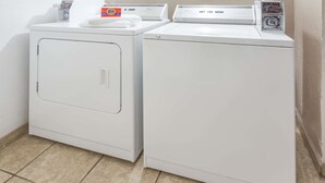 Un área de lavandería con dos lavadoras blancas y una caja de detergente Tide sobre la lavadora de la izquierda.