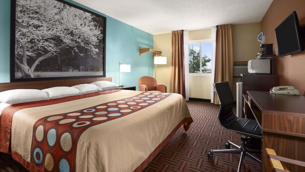 A hotel room with a large bed, a desk with a chair, a television, and a window with curtains.