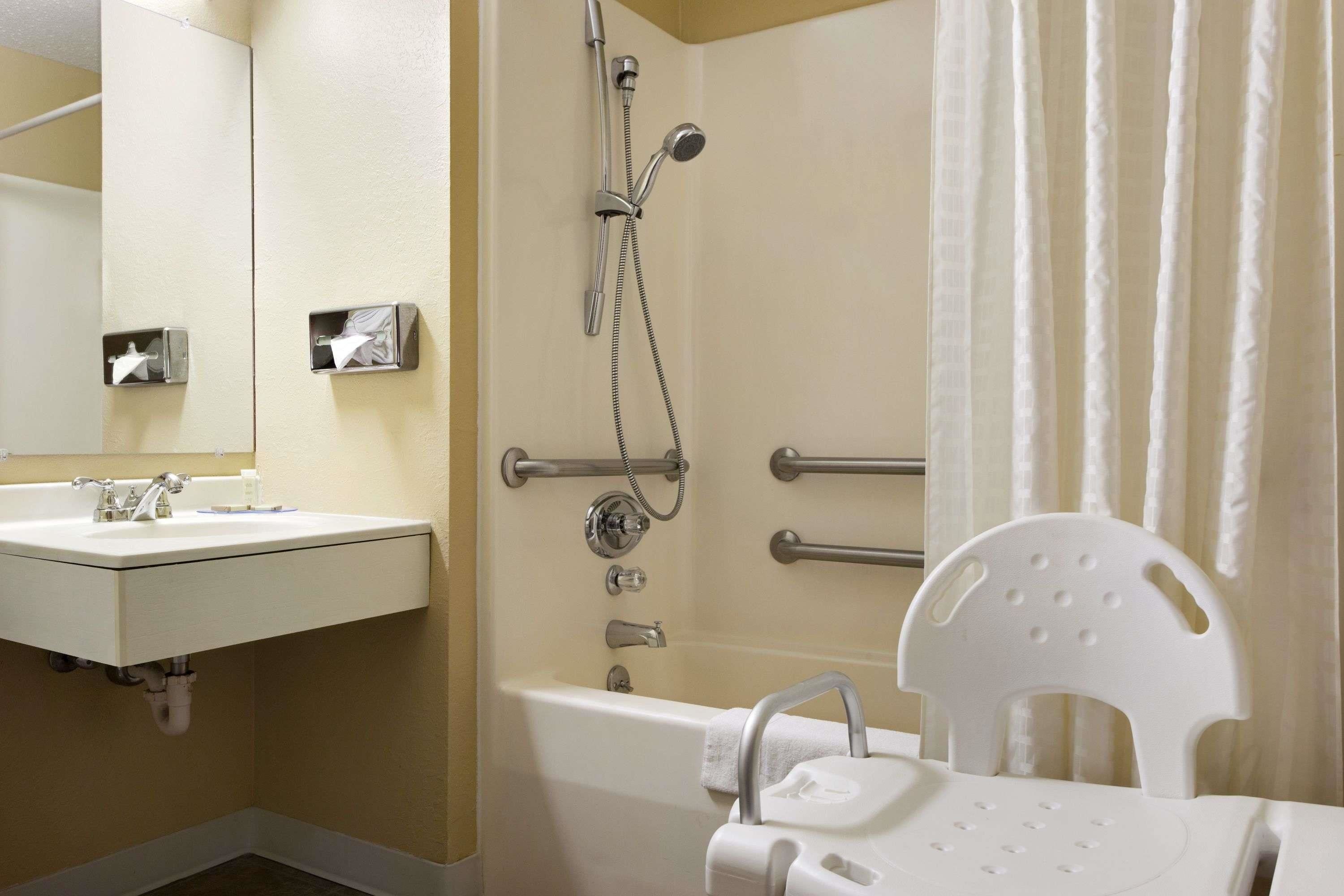 A bathroom with a sink, mirror, shower, and grab bars.