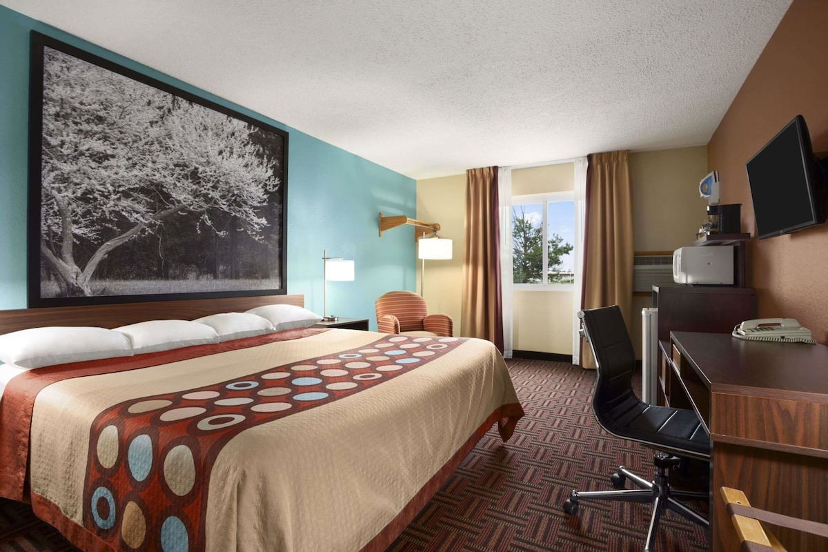 Una habitación de hotel con una cama grande, un escritorio, una silla, un televisor y una ventana con cortinas.