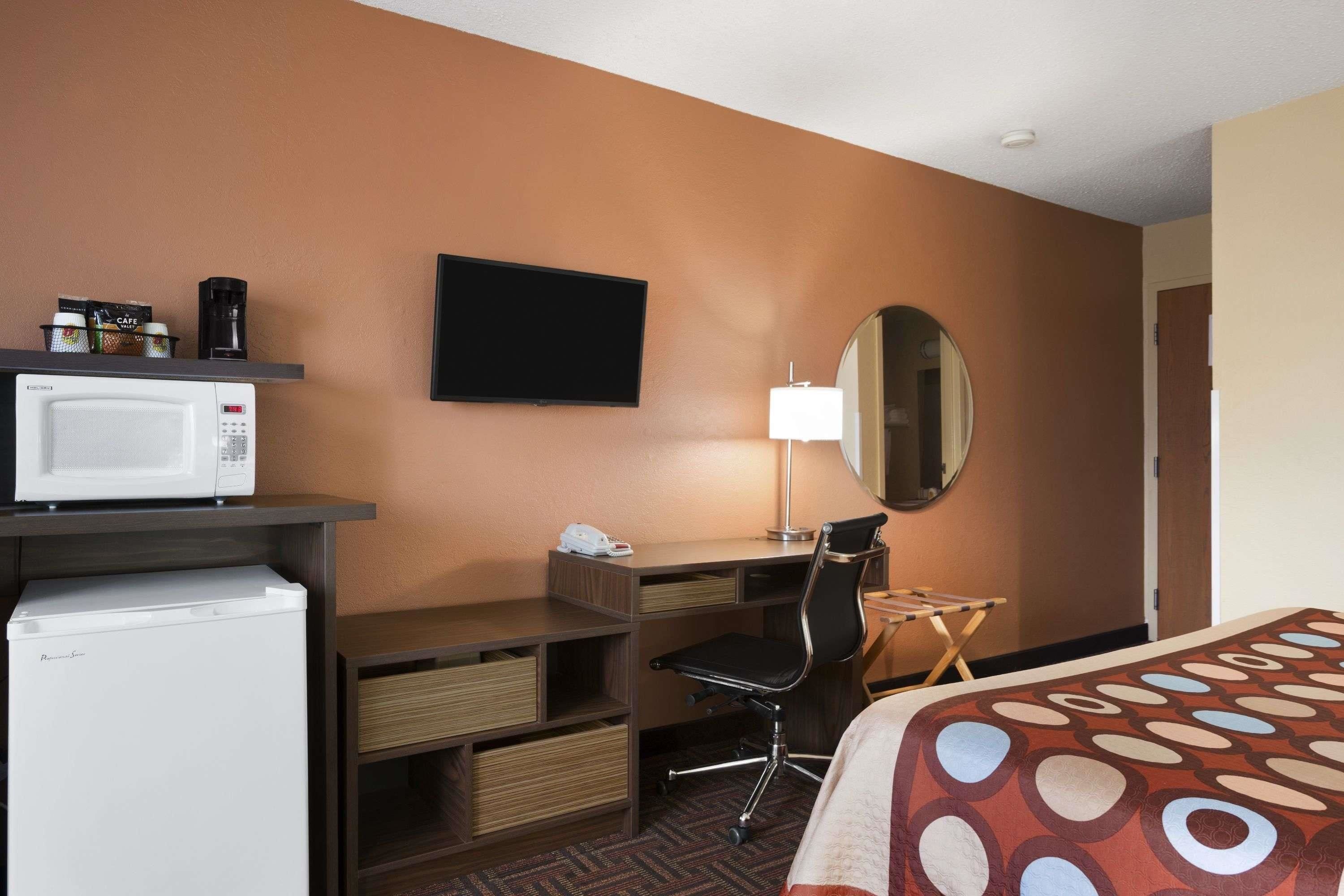 A hotel room with a bed, a desk with a chair, a microwave, a coffee maker, a TV, and a mirror.