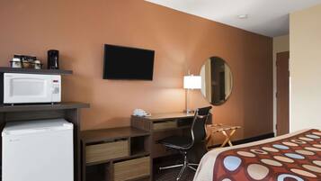 Habitación de hotel con cama, escritorio con silla, microondas, cafetera, televisión y espejo.