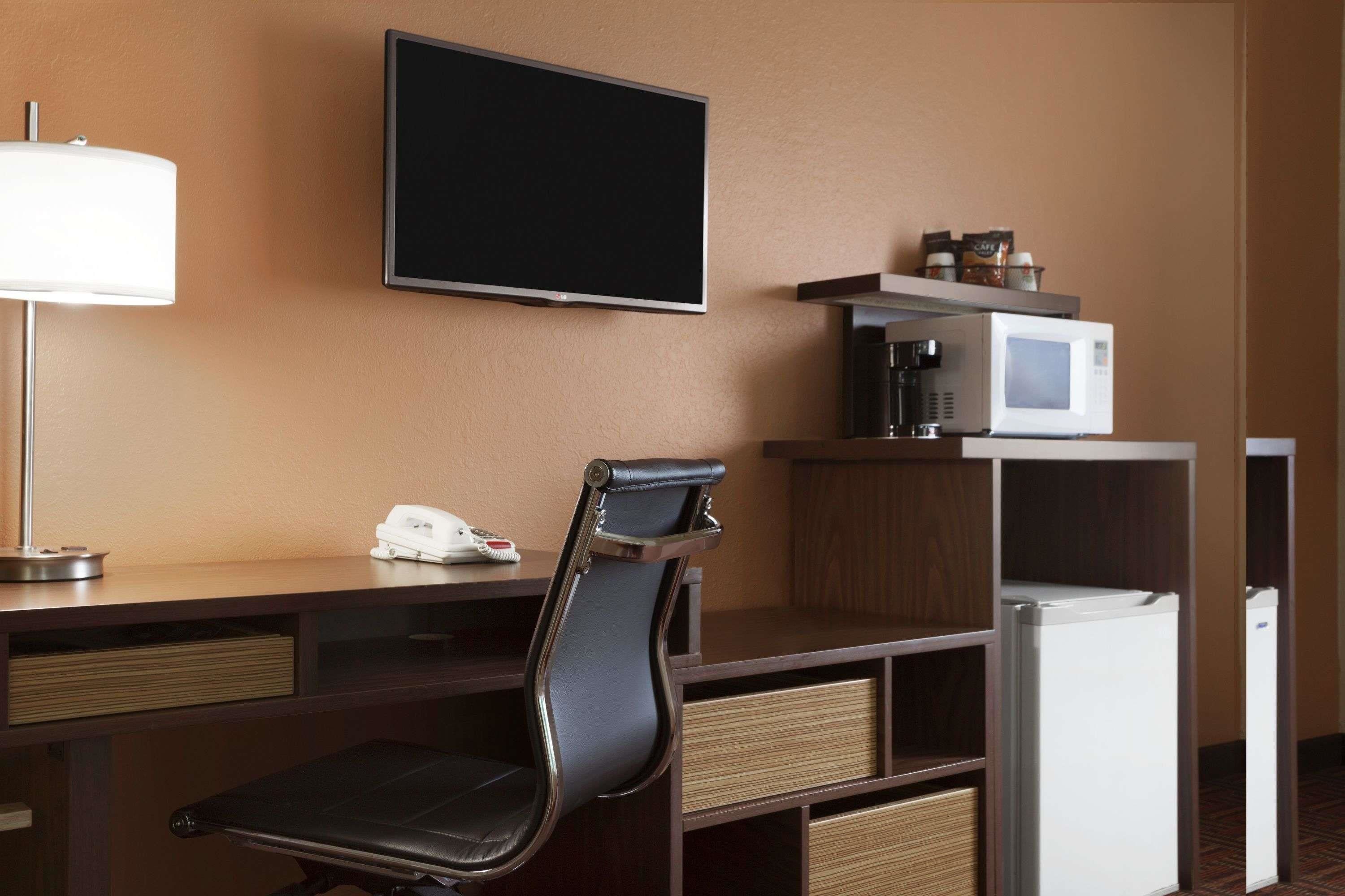 A hotel room with a desk, a chair, a television, a microwave, a refrigerator, and a coffee maker.