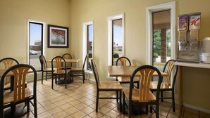 A dining area with wooden tables and chairs, framed artwork on the walls, and a window view.
