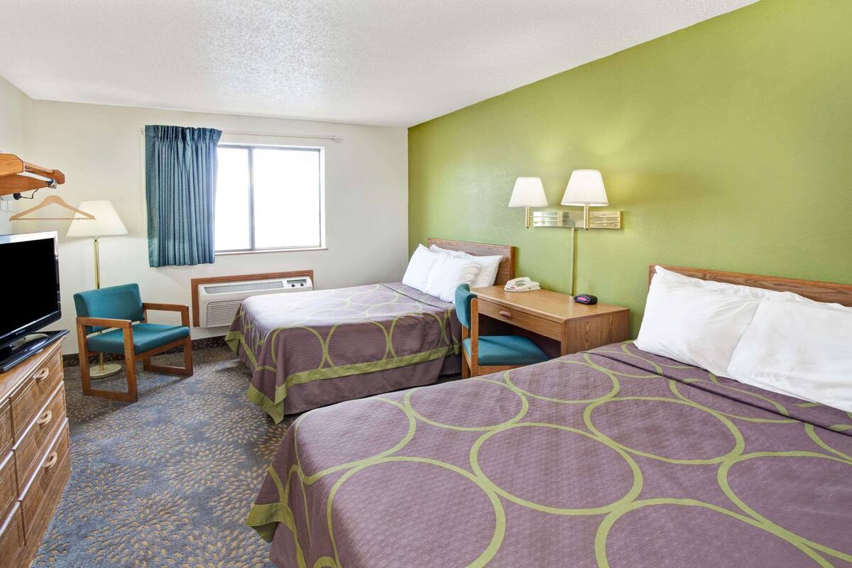 A hotel room with two beds, a desk, a chair, a TV, and a window with curtains.