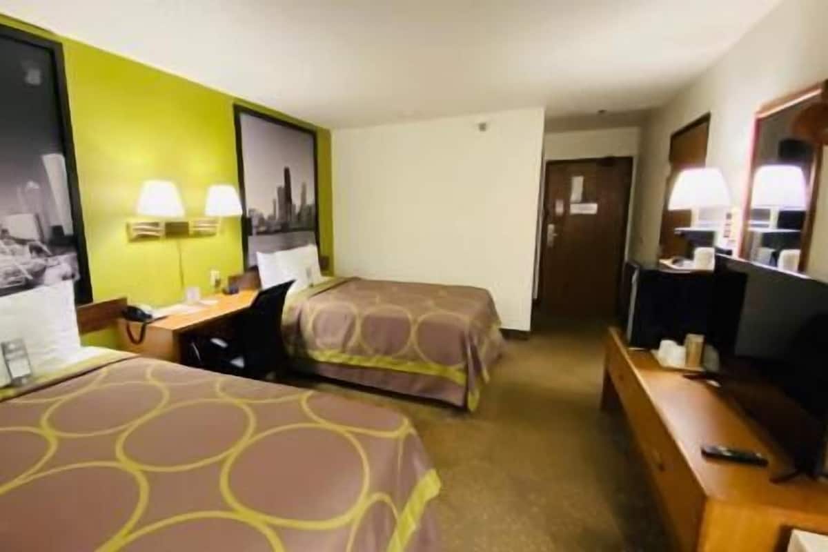 A hotel room with two beds, a desk, a chair, a television, and a mirror.