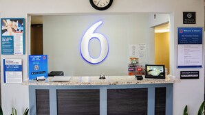 A reception desk with a large illuminated number 6, a clock above it, and various informational posters and signs around the area. - Motel 6 Litchfield, IL (Litchfield)