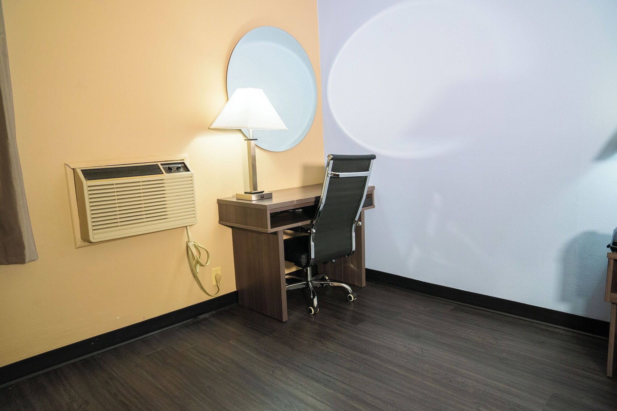 Habitación de hotel con escritorio, silla, lámpara, unidad de aire acondicionado y una gran proyección en la pared.
