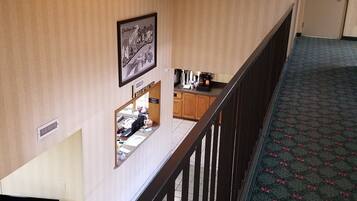 A hotel room with a desk, a chair, a ceiling fan, a registration desk, and a carpeted floor.