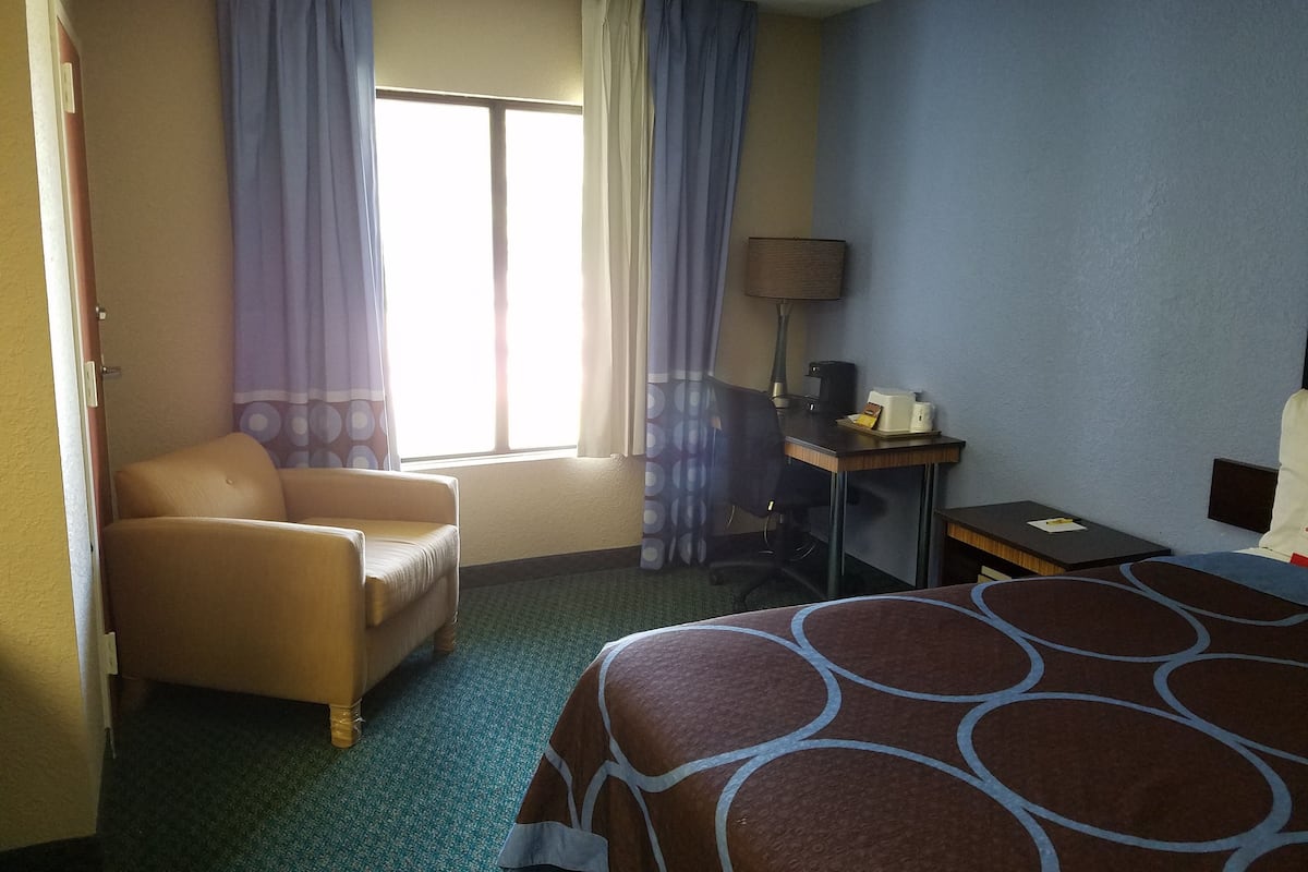 A hotel room with a bed, a desk, a chair, and a window with curtains.