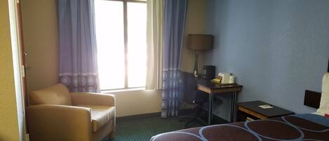 A hotel room with a bed, a desk, a chair, and a window with curtains.