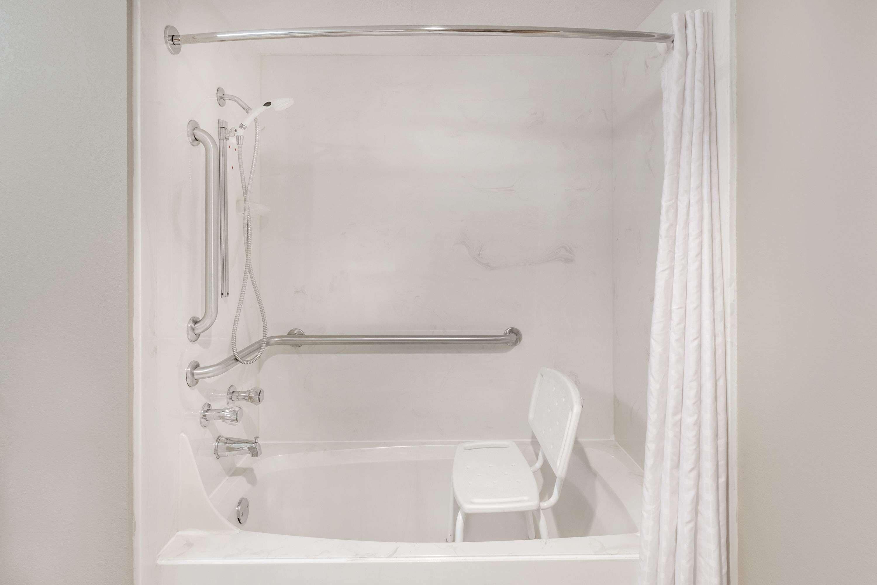 Una ducha blanca con una barra de apoyo, una silla blanca y una bañera.