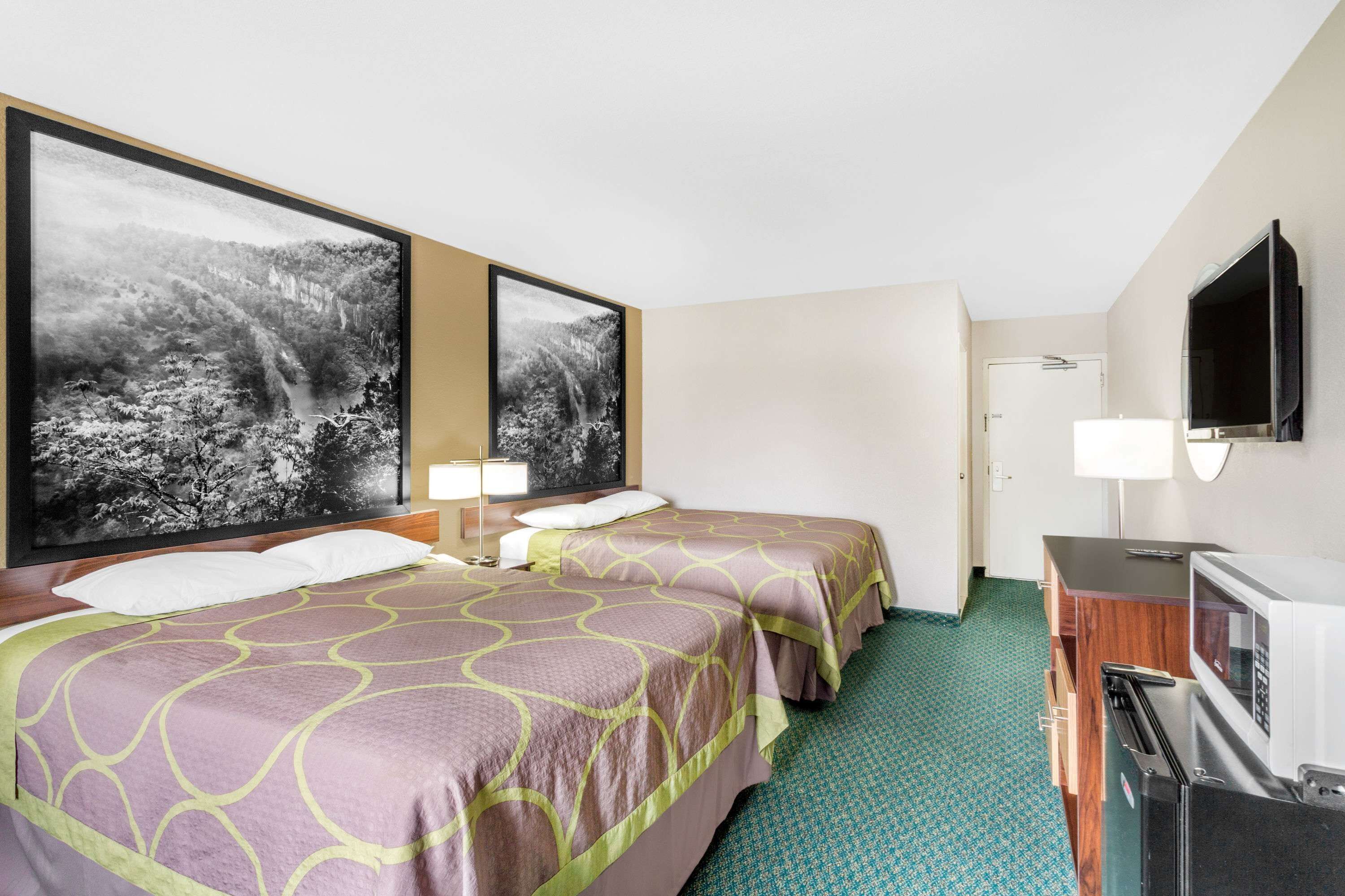 A hotel room with two beds, a TV, a desk, and a microwave.