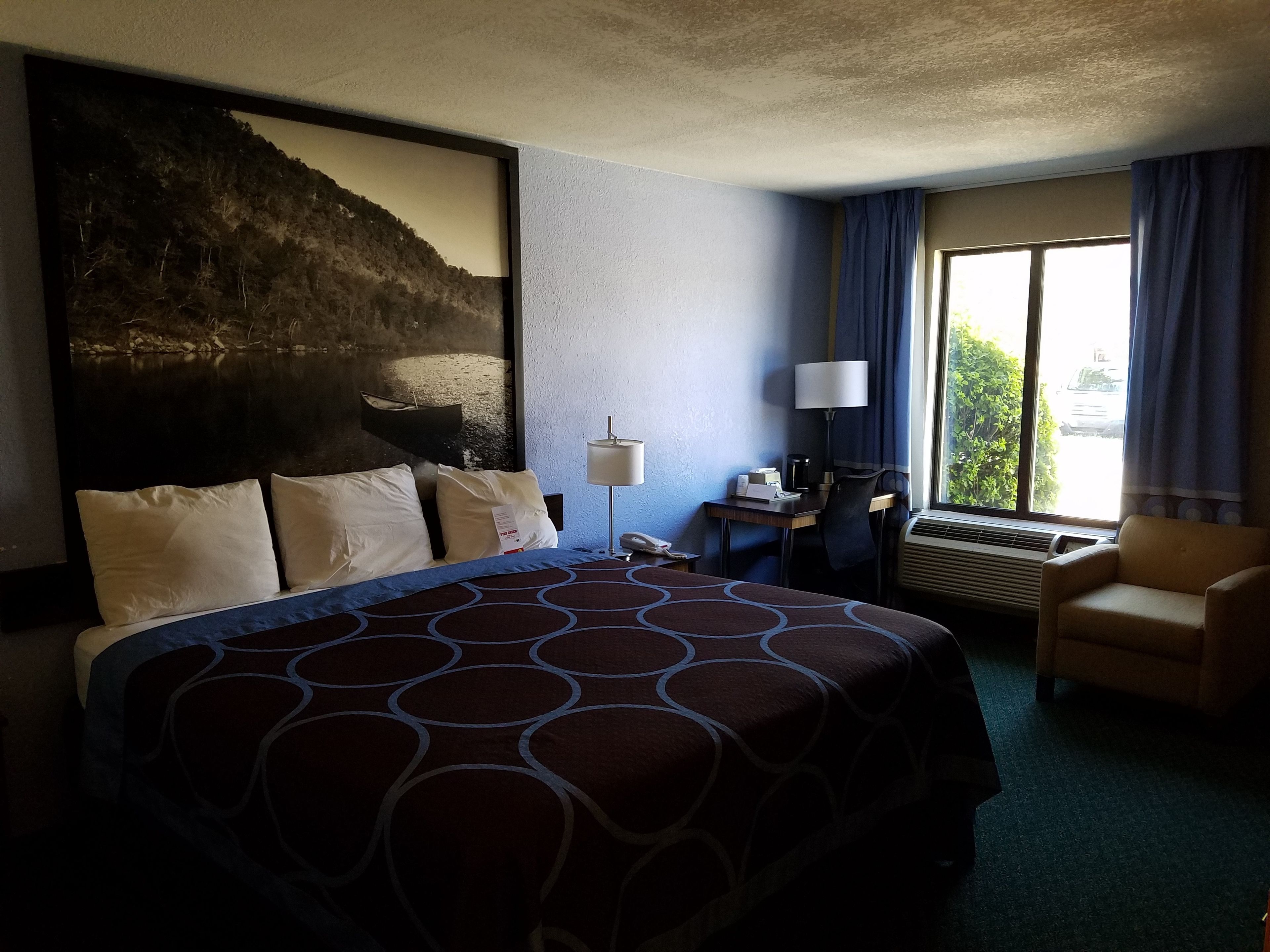 Habitación de hotel con una cama grande, un escritorio con lámpara, una silla y vistas al exterior.