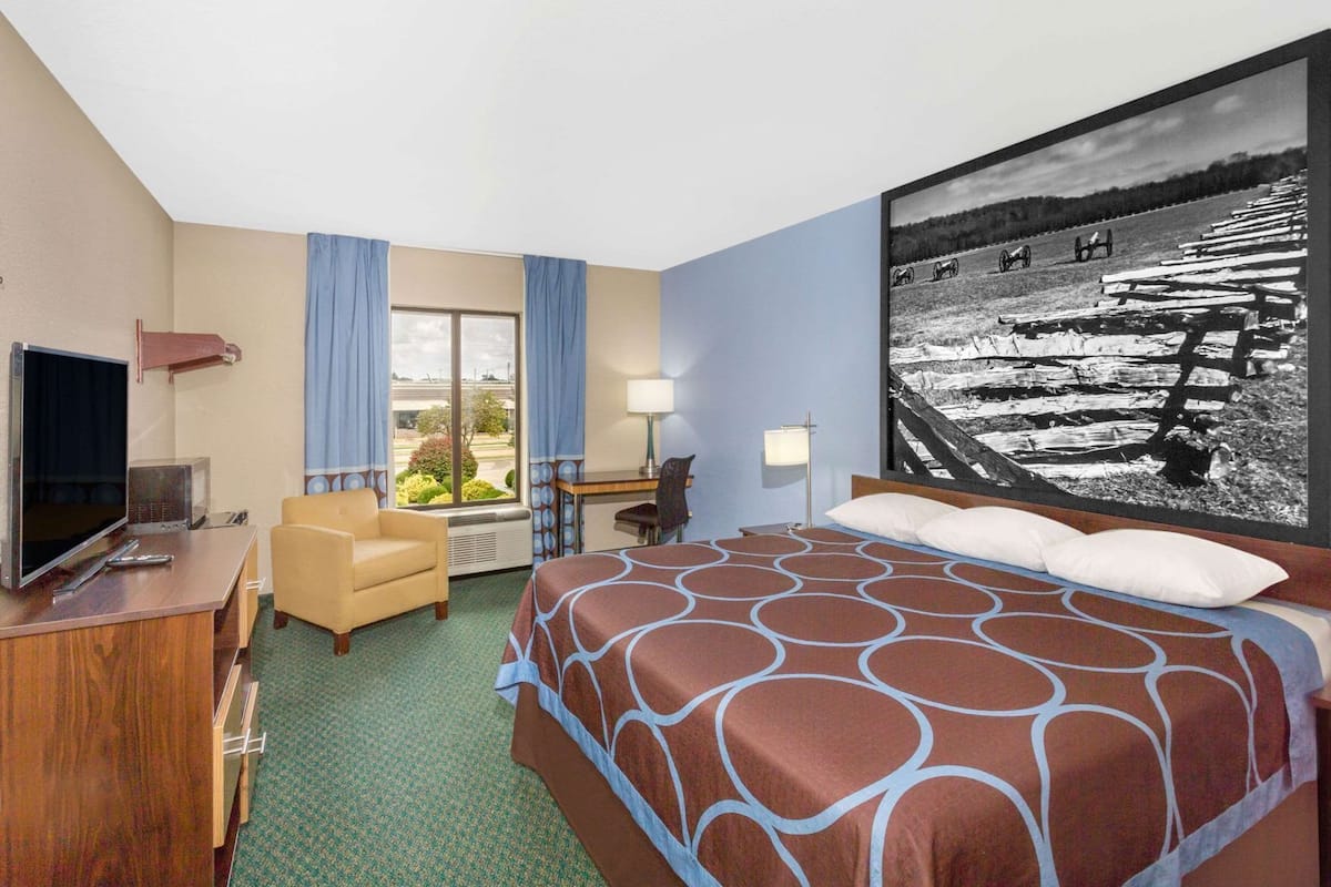 A hotel room with a bed, a desk, a chair, a television, and a large window.