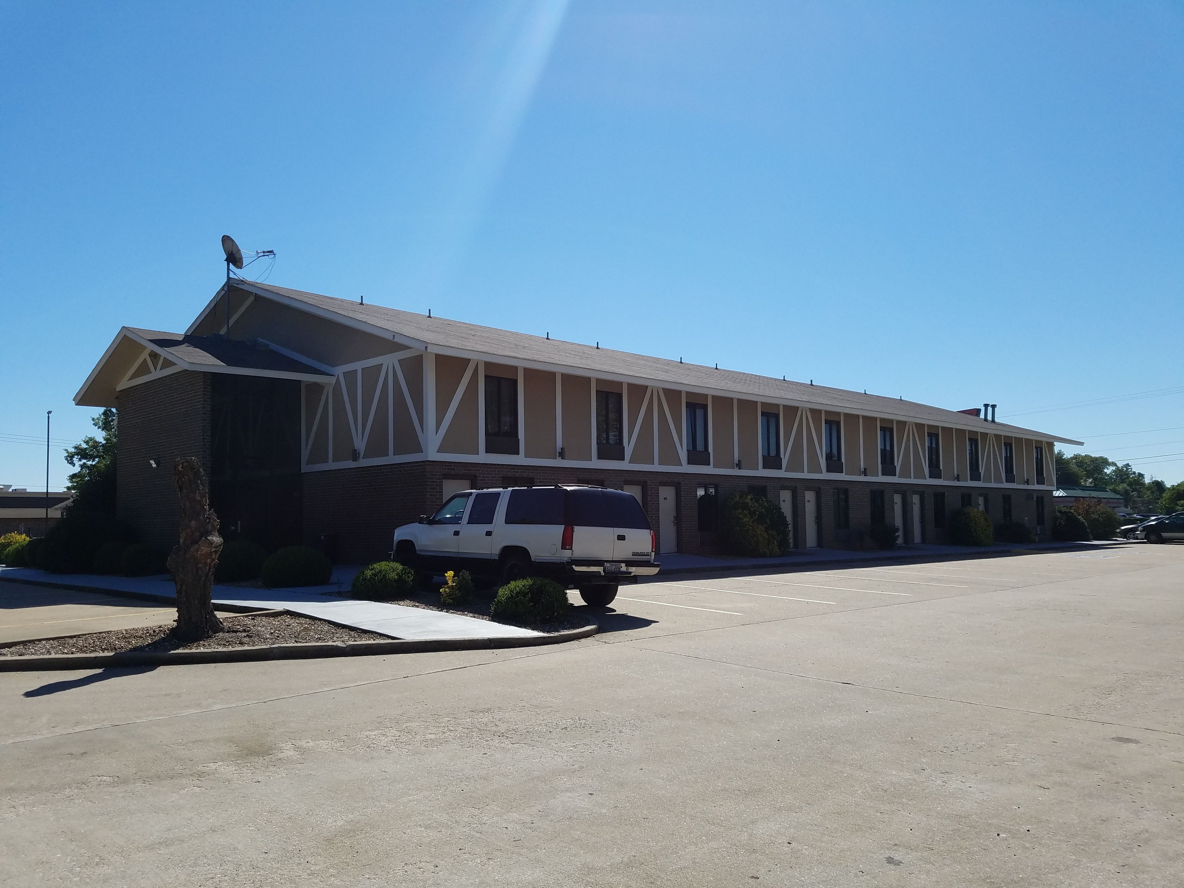 Un motel composé d’un bâtiment d’un seul étage, d’un espace de stationnement couvert et d’un VUS blanc garé devant.