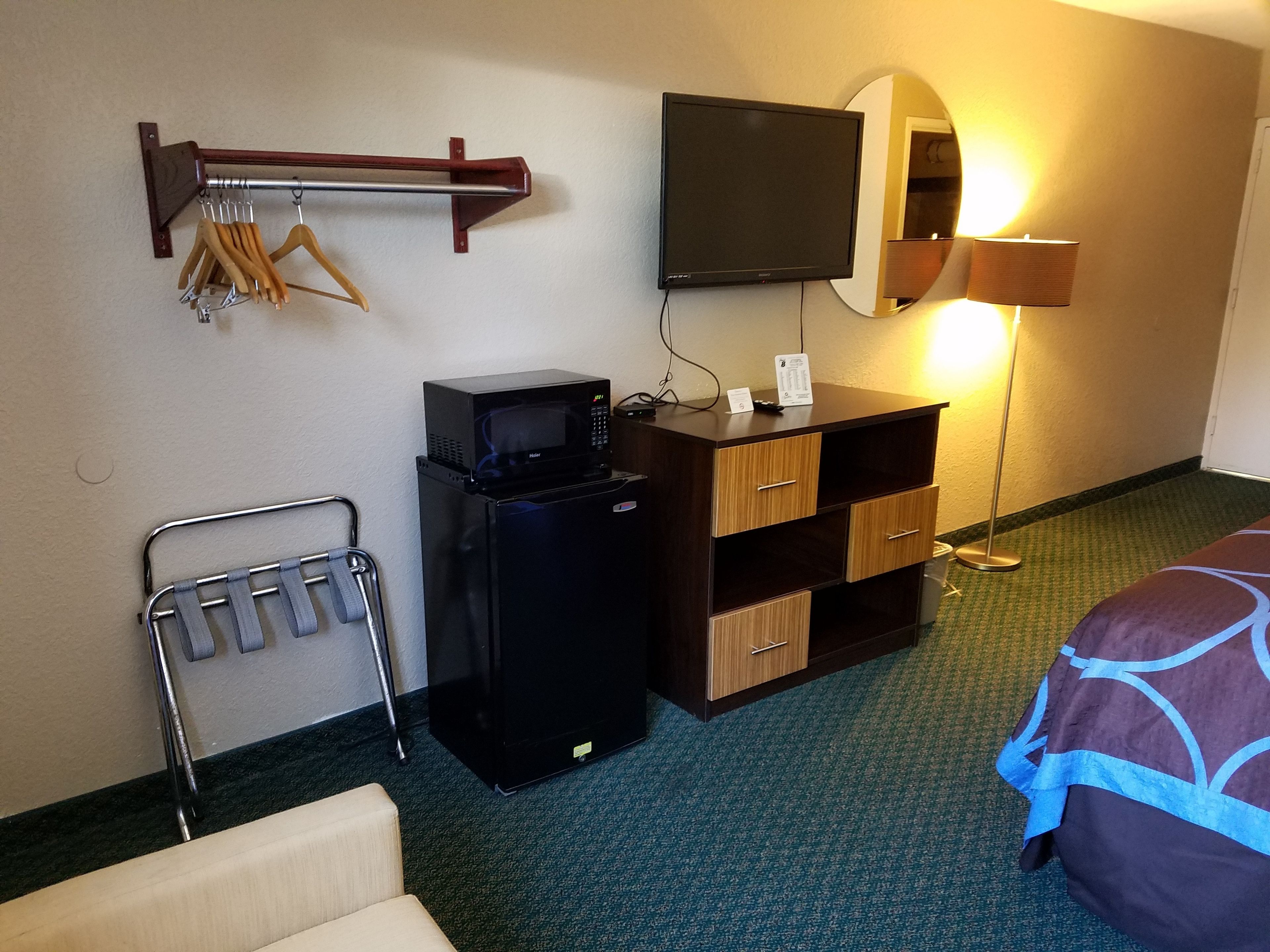 Une chambre d’hôtel équipée d’un téléviseur à écran plat fixé au mur, d’un minibar, d’un bureau avec un miroir et d’un lit recouvert d’une couvre-lit à motifs.