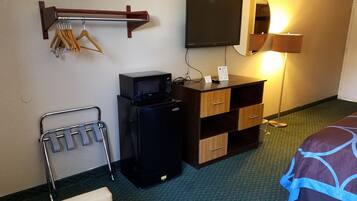 Une chambre d’hôtel équipée d’un téléviseur à écran plat fixé au mur, d’un minibar, d’un bureau avec un miroir et d’un lit recouvert d’une couvre-lit à motifs.