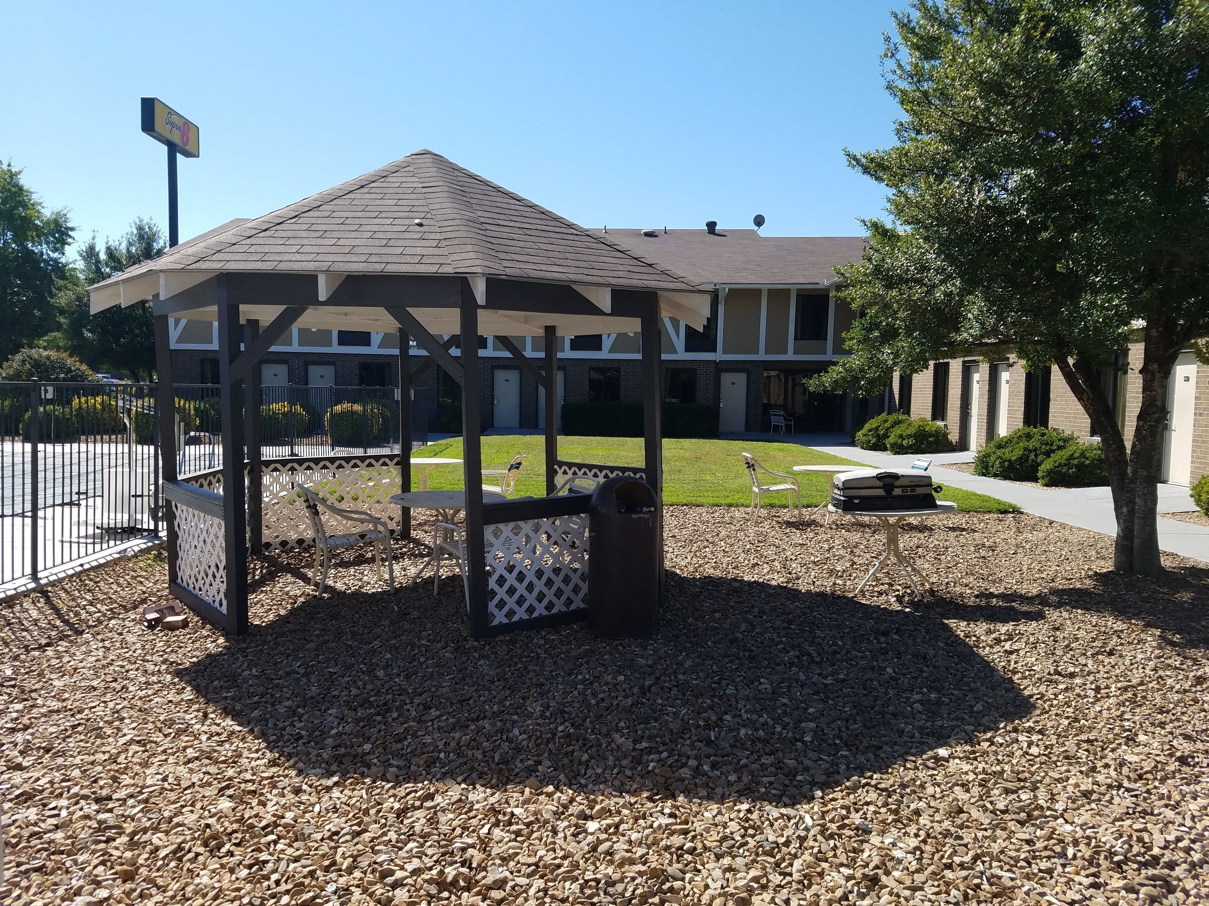 A gazebo with a roof, surrounded by a gravel area and white lattice fence.