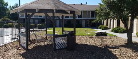A gazebo with a roof, surrounded by a gravel area and white lattice fence.