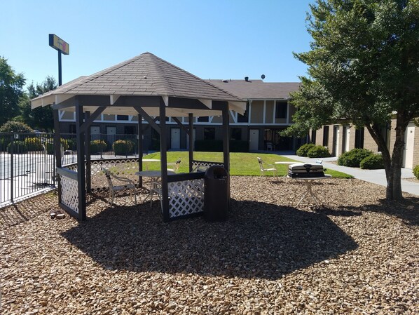 A gazebo with a roof, surrounded by a gravel area and white lattice fence.