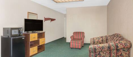 A compact room with a kitchenette, a flat-screen TV, a floral-patterned armchair, and a wooden cabinet.