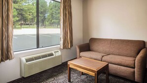 Ein Zimmer mit einer Couch, einem kleinen Tisch, einem Fenster mit Vorhängen und einer Wand-Klimaanlage.