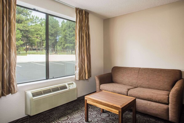 A room with a sofa, a small table, a window with curtains, and a wall-mounted air conditioner.