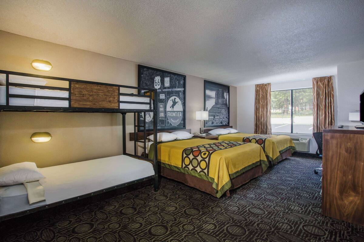 Una habitación de hotel con literas, un escritorio y un ventanal grande con cortinas.