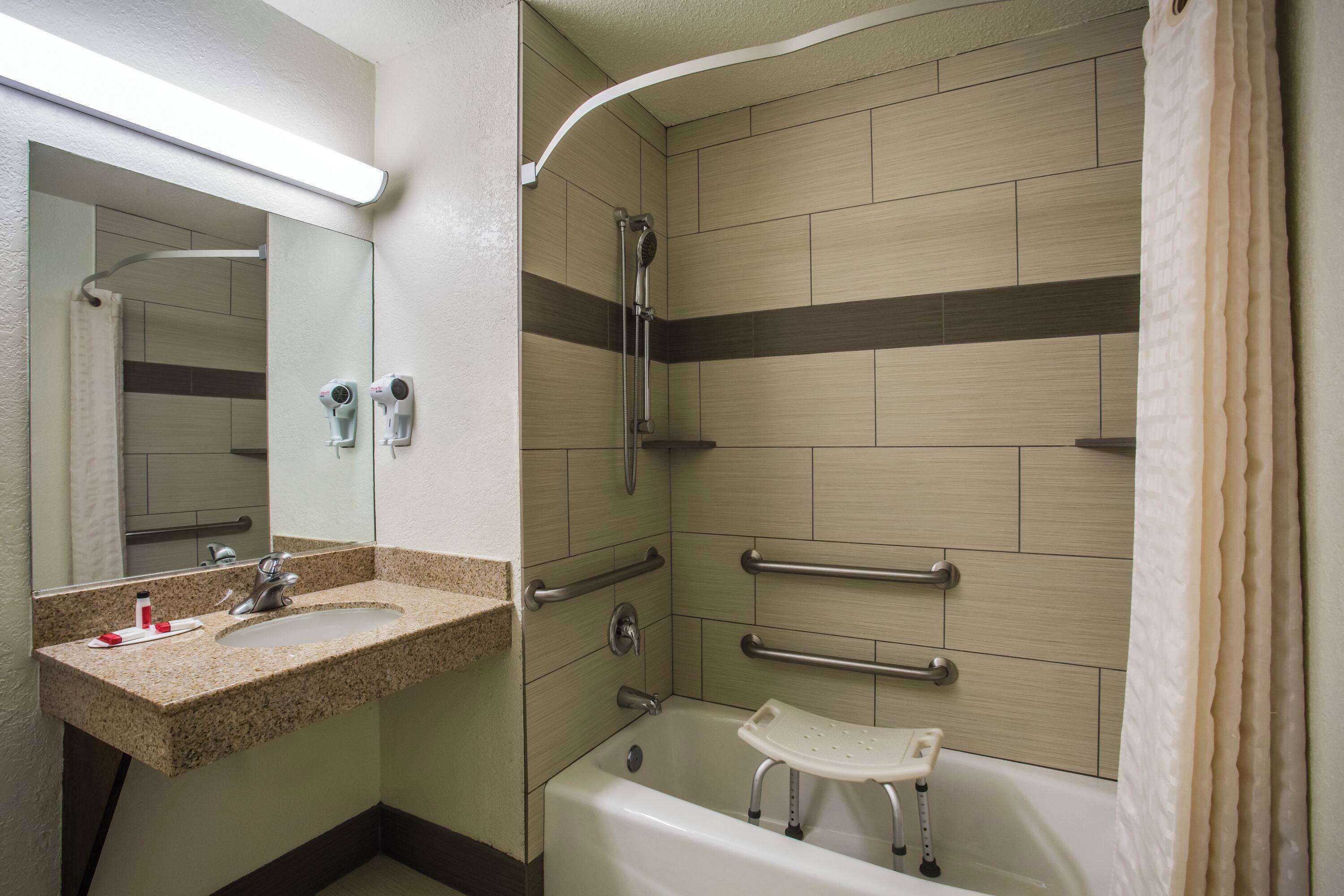 A bathroom with a sink, mirror, shower, and grab bars.