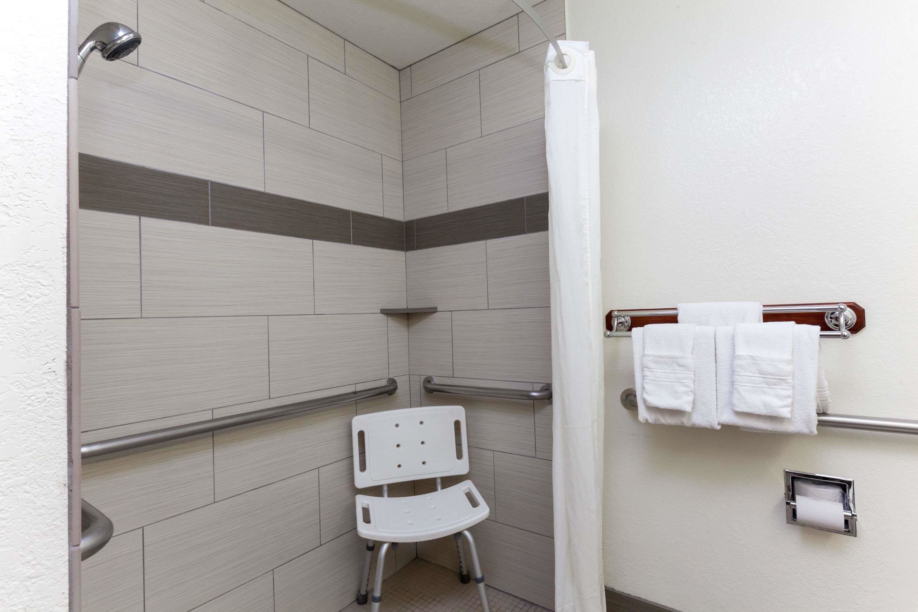 A handicap-accessible shower area with a white chair, grab bars, and a towel rack.