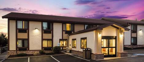 A hotel with a parking lot, a covered entrance, and a building with multiple windows and a flat roof.