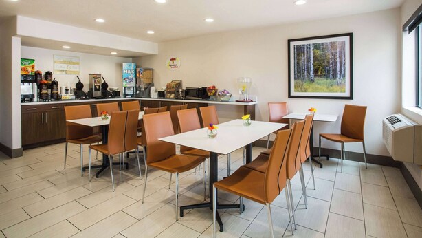 Ein moderner Essbereich mit einem weißen Tisch und braunen Stühlen, ein Küchenbereich mit verschiedenen Geräten und einem gerahmten Bild an der Wand.
