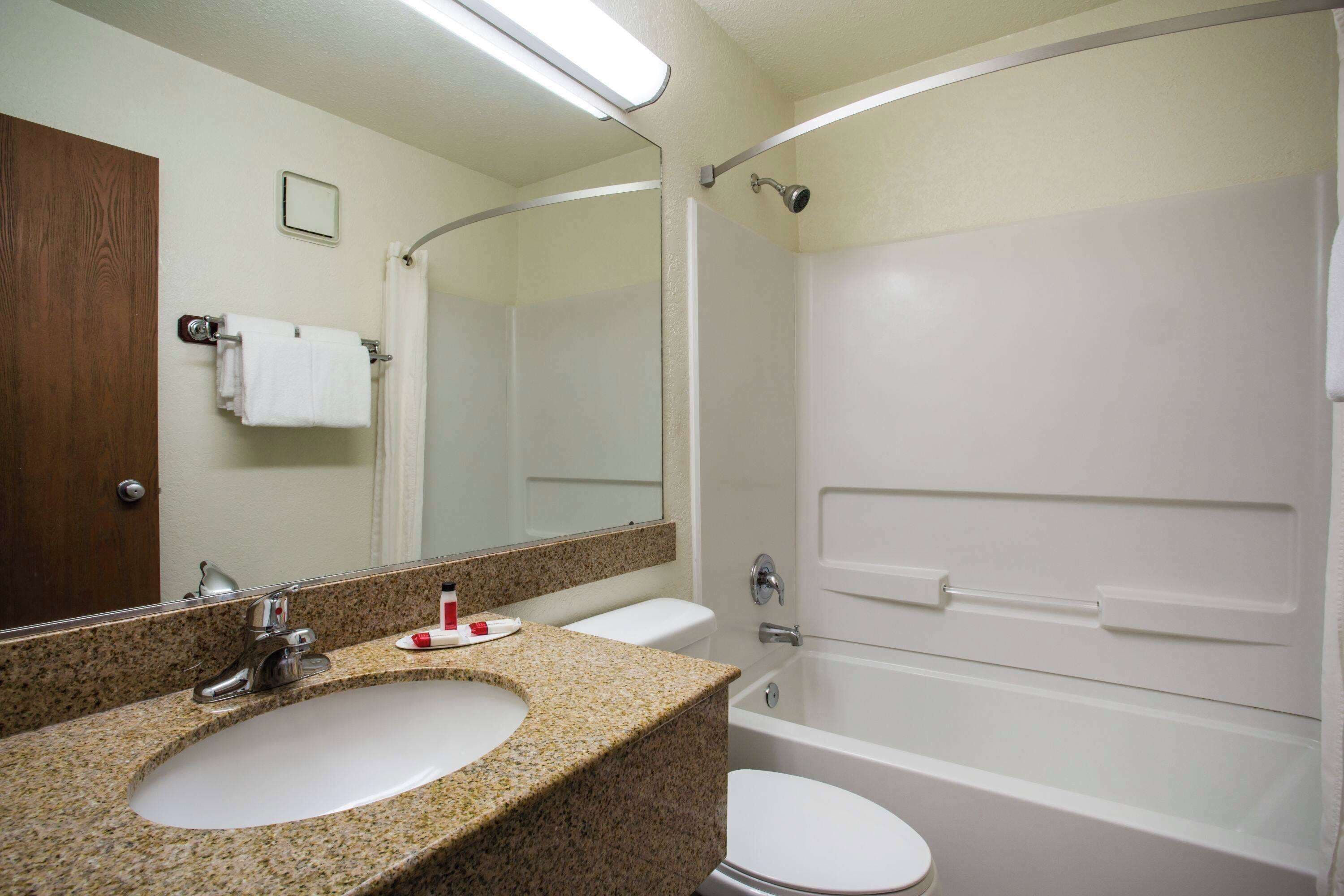 A bathroom with a granite countertop sink, a white toilet, a bathtub, and a mirror.