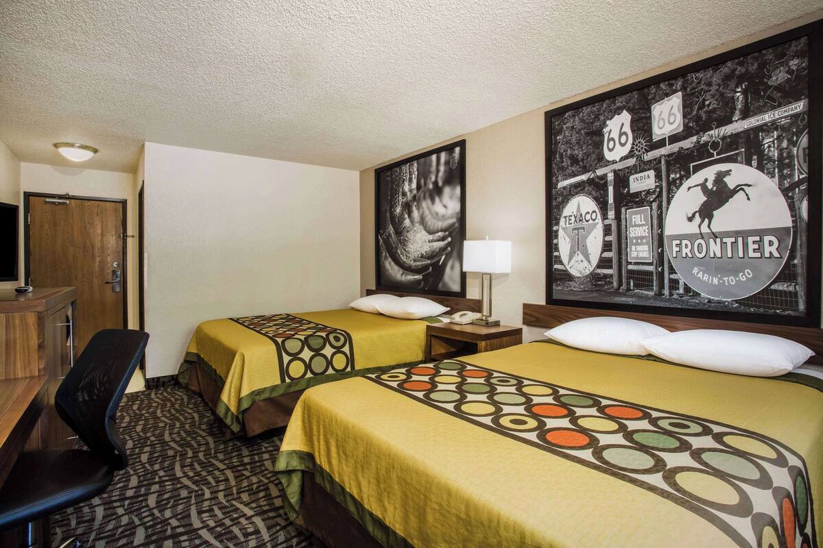 Habitación de hotel con dos camas, un escritorio, una silla y un mural grande en la pared.