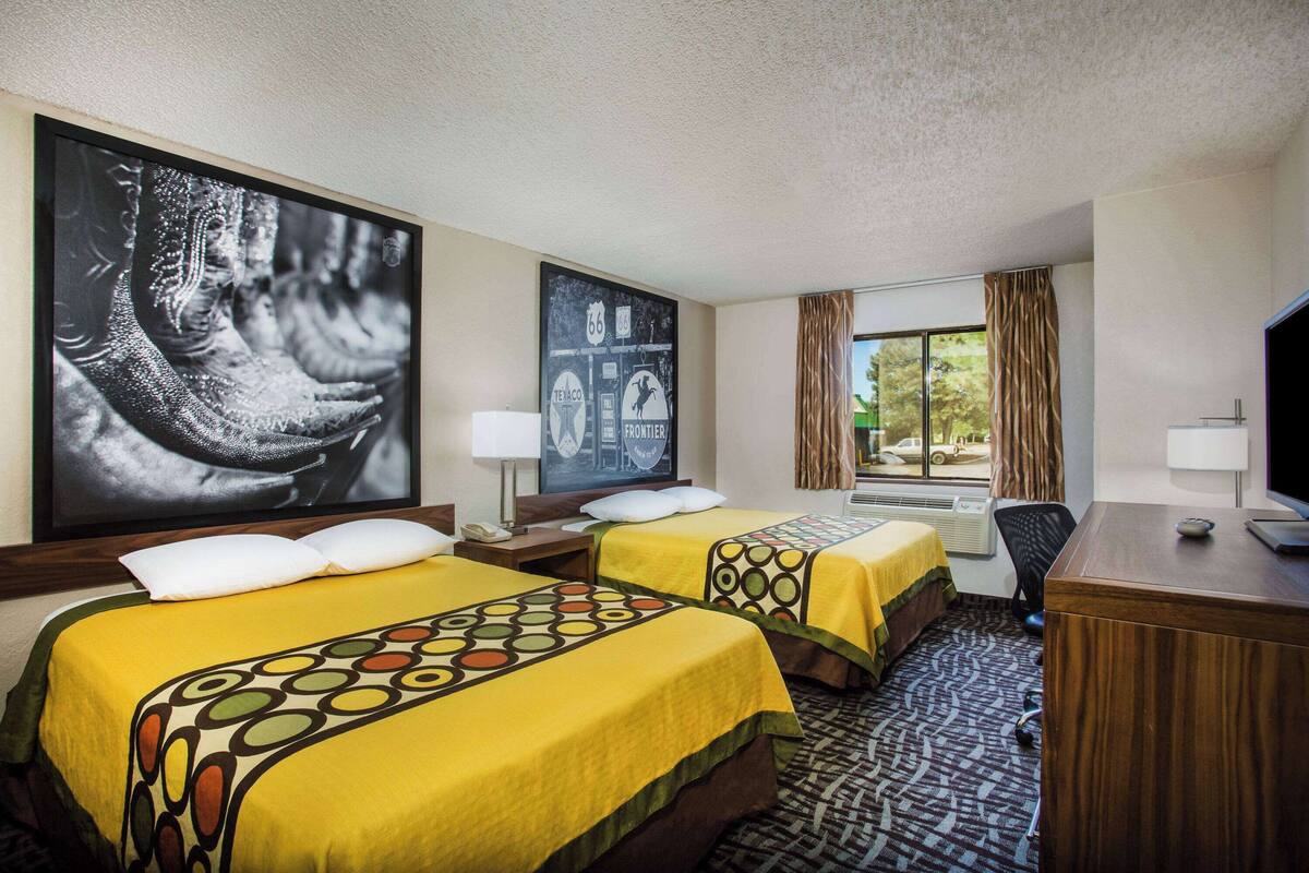 Una habitación de hotel con dos camas, un escritorio, una silla, un televisor y una ventana con cortinas.