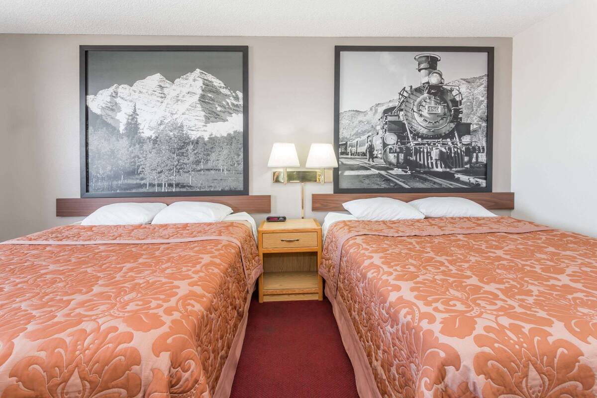 A hotel room with two beds, a nightstand with a lamp, and two framed pictures on the wall.