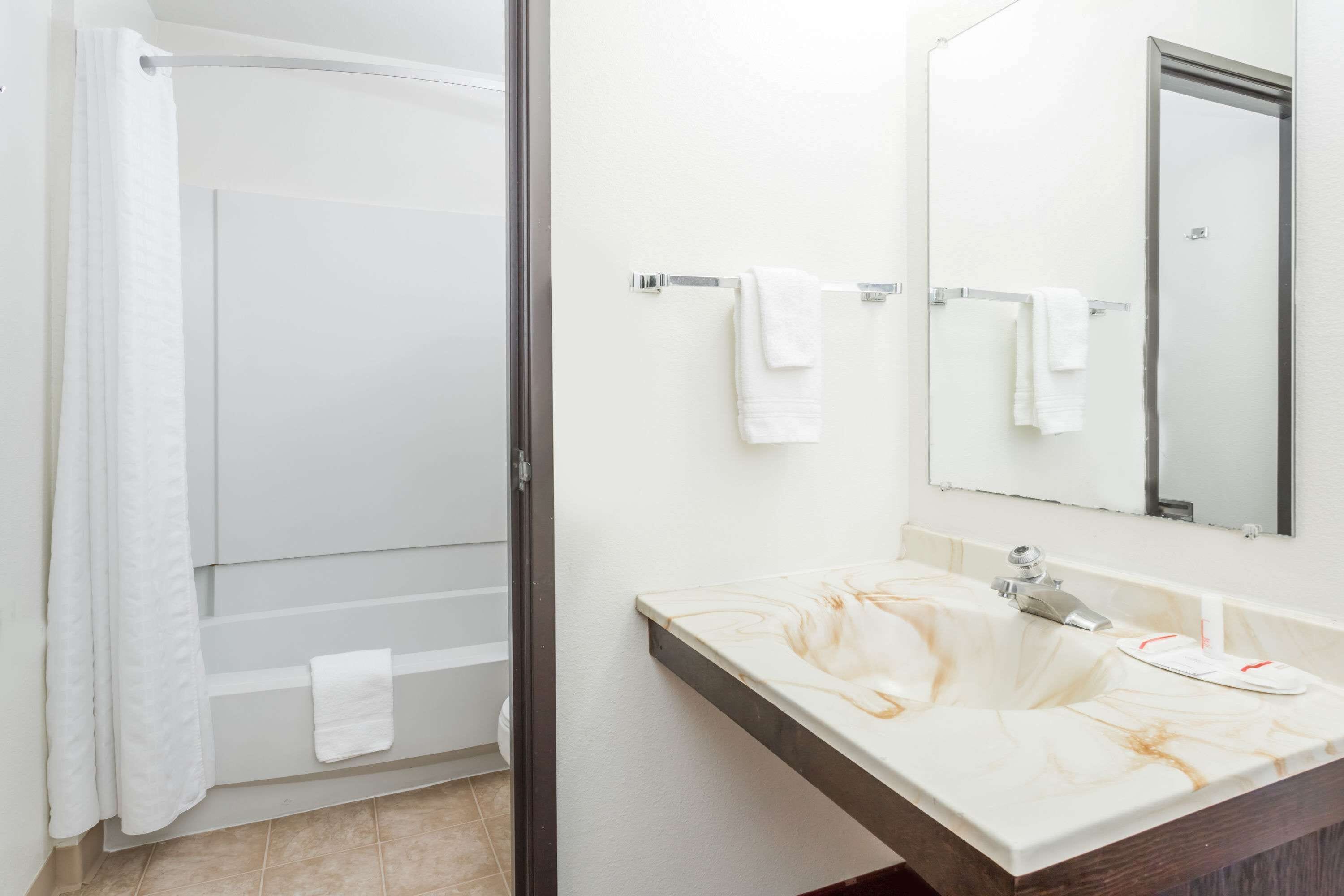 Un baño con ducha, un lavabo con encimera de mármol y un espejo sobre el lavabo.