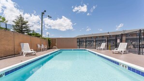 A rectangular swimming pool with a blue tiled edge, surrounded by white lounge chairs and a metal fence. - Super 8 by Wyndham Grand Junction Colorado (Grand Junction)